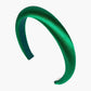 The Tori Satin Headband shimmers in a vibrant emerald green with a padded design and a smooth satin finish. Its interior is lined with a slightly darker green fabric, adding to its luxurious charm. Set against a plain white background, this headband effortlessly elevates any outfit with its elegant silk touch.