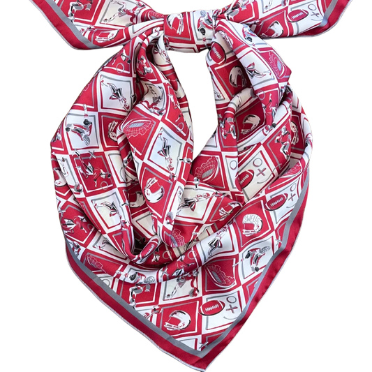 The Gameday Scarf - Crimson & Grey Checkerboard is a handmade piece featuring a sports-themed pattern with footballs, baseball bats, and helmets arranged in a geometric design. Neatly tied in a knot, this vibrant Montreal scarf beautifully showcases its intricate design.