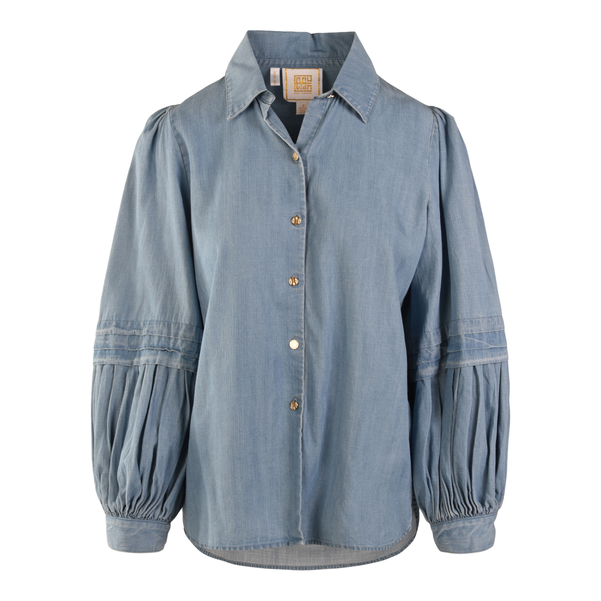 The Oxford blouse features light blue denim chambray, a collared neckline, button-down front, and long balloon sleeves with gathered detailing. Its relaxed fit and slightly curved hem give it a modern twist.