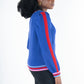 A person with curly hair is wearing the Clara Cardigan - Bauhaus Stripe in bright blue, showcasing red and pink striped sleeves and hem. The puff sleeves add a distinctive flair as they pose sideways against a plain white background. Gold button closures enhance the stylish appearance.