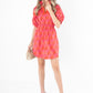 A woman stands against a white background, dressed in a lively red Palmer Dress - Block Monogram featuring a ruffle cinched waist, paired with beige platform sandals. Her long hair is styled with a coordinating red headband, and she carries a woven clutch.