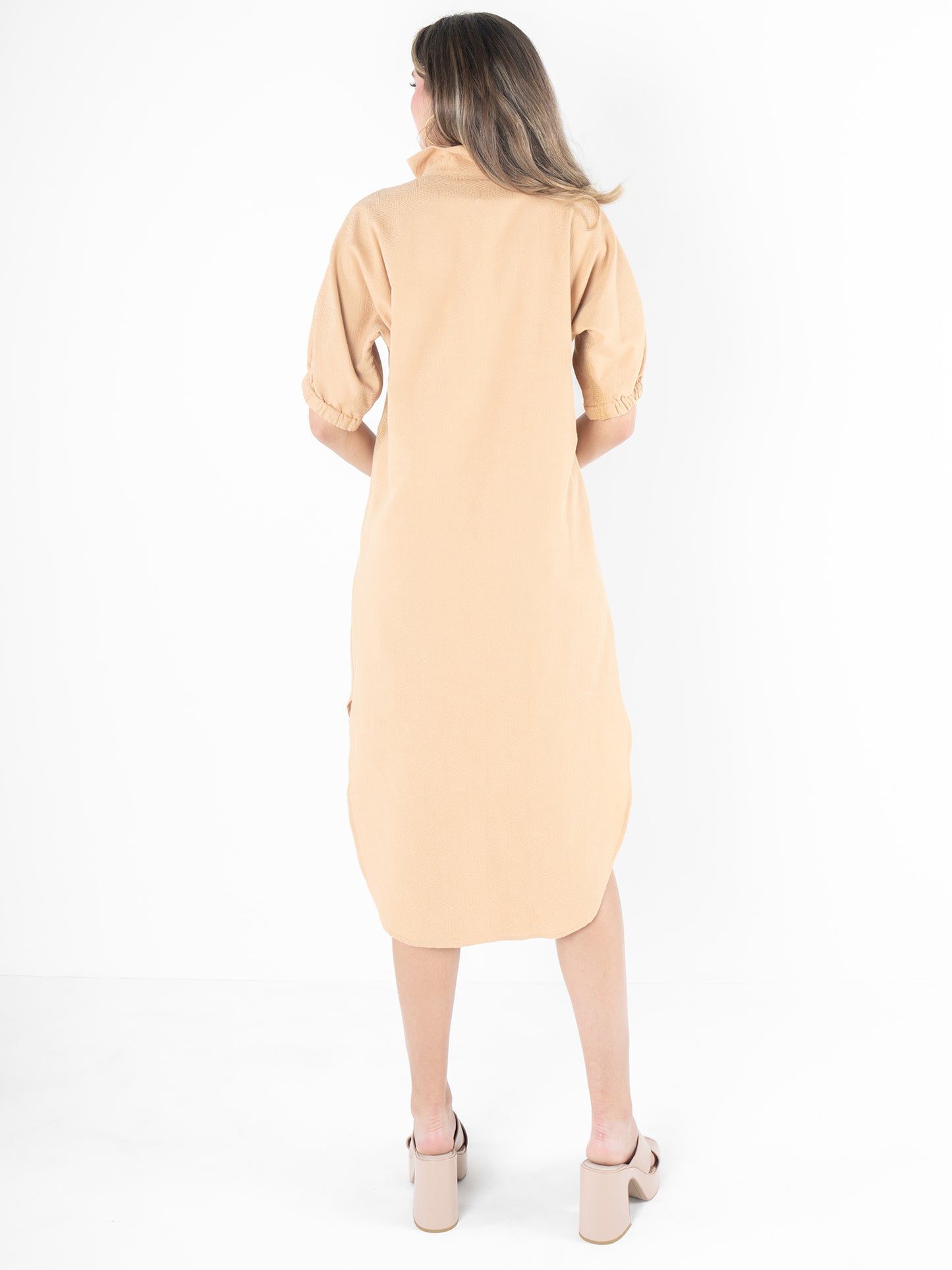 From behind, a person with long hair is pictured wearing a relaxed silhouette that includes the beige-collared Poppy Caftan - Lark Monogram and beige platform sandals. They are standing against a white background.