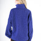 A woman with long blonde hair wears the Poppy Pop-Over in Royal Blue Cheetah, featuring a high collar and embossed fabric. She stands with her back to the camera against a plain white background, her long sleeves adding elegance to the ensemble.