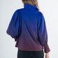 A person with long hair is wearing the Charlotte Top - Midnight Ombre, which showcases an ombre effect in purple with puff sleeves and a ruffled collar. They are turned away from the camera, paired with black pants, against a simple light background.