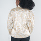 A person with dark curly hair wears the Orchid Top in a neutral freckle spot cheetah print, exuding feminine style. Their back faces the camera, highlighting the blouson long sleeves against a plain background.