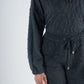 A person is wearing the Poppy Pop-Over in Jet Black Cheetah, a textured long-sleeve jumpsuit made from embossed cheetah fabric featuring a distinct pattern and drawstring waist, as they pose against a simple light background. The image highlights the upper half of their body and right arm.