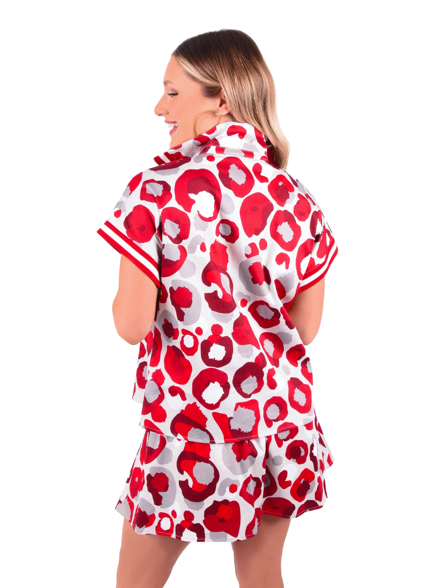 A woman with long hair is facing away, wearing a Poppy Pullover in Burgundy Collegiate Cheetah and a matching skirt adorned with bold circular patterns. The dolman sleeves enhance the design against the plain white background.