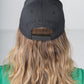 A person with long, wavy hair is seen sporting a black Emily McCarthy Signature Hat, featuring her name elegantly embroidered on the back. They pair this stylish cap with a comfortable green shirt while standing against a neutral gray background.