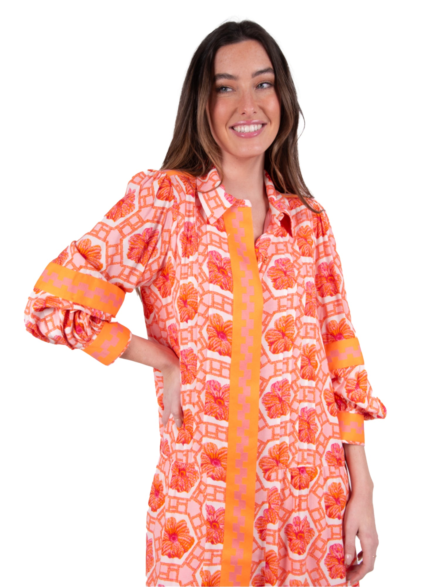 A person with long hair smiles while wearing the Delany Dress - Floral Crochet, designed in an orange and pink floral pattern with yellow accents. Set against a plain white background, this ensemble offers a vintage touch while exuding modern elegance.