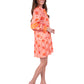 The person with long hair is smiling and standing sideways, exuding modern elegance in a vibrant orange patterned Delany Dress - Floral Crochet with long sleeves. They pair it perfectly with beige platform sandals, all set against a plain white backdrop.