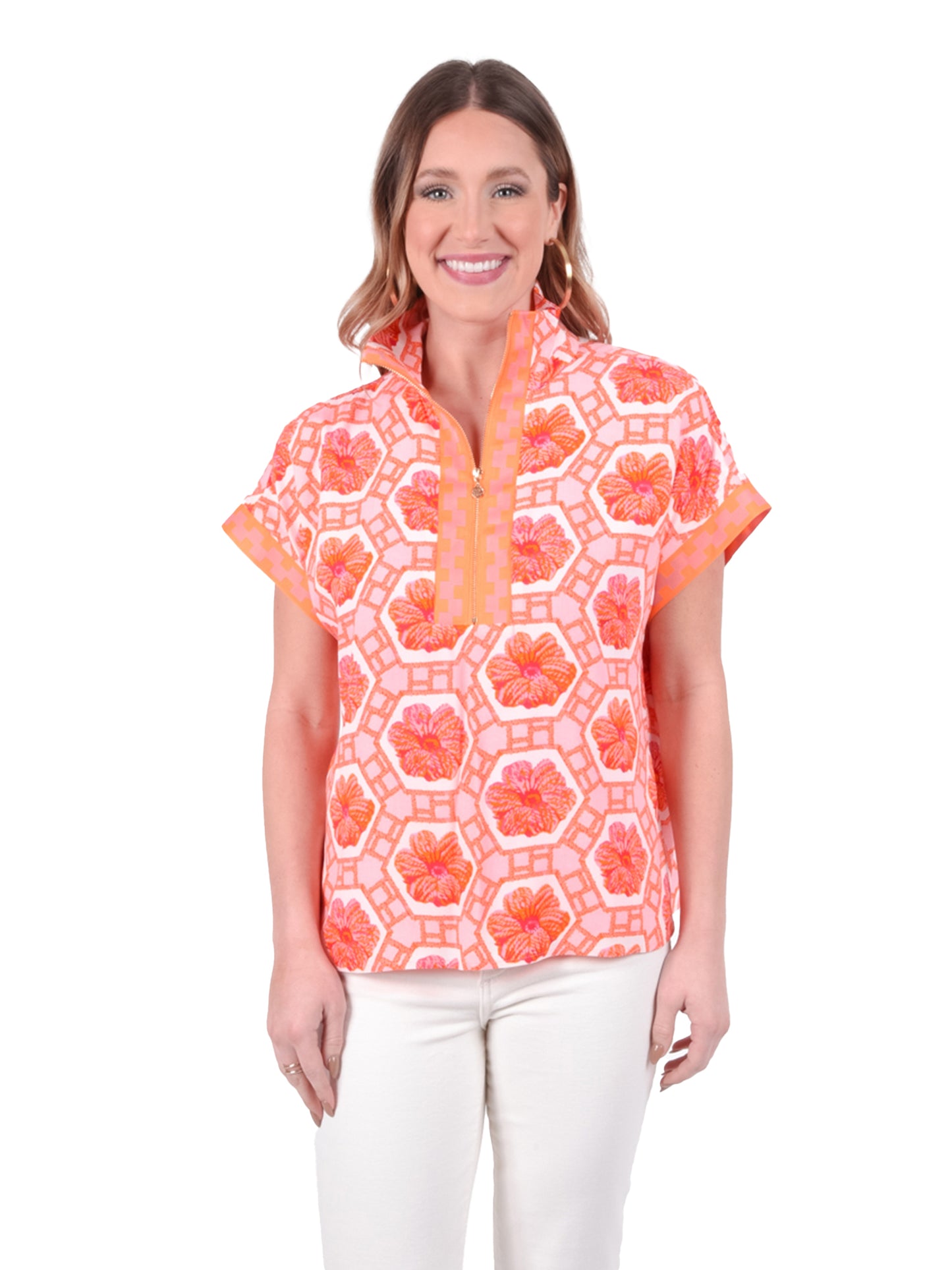 A person wearing the vibrant Poppy Pullover - Floral Crochet by Emily McCarthy, showcasing a lively mix of geometric and floral designs in hues of orange and pink, pairs it with light-colored pants. They beam at the camera against a white backdrop, their colorful outfit radiating joy.