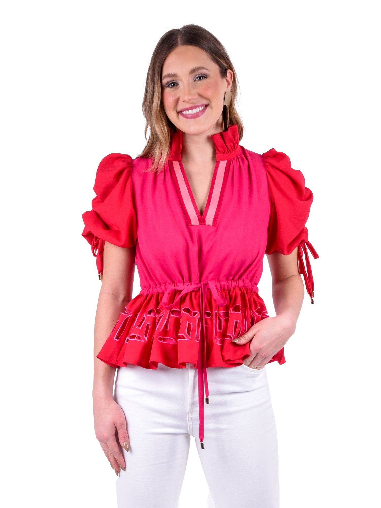 A person with long hair smiles while posing against a white background, wearing the Posey Top in Cabaret, which features puff sleeves and is paired with white pants.