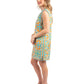 A woman stands sideways in an Emily Shift Dress - Poolside, showcasing a vibrant Amalfi Coast print with hues of blue, orange, and green. She pairs it with nude platform heels and has long, wavy hair. Her gentle smile is set against a plain white background.