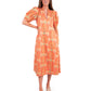 A person stands wearing the Hampton Dress - Cloister by Emily McCarthy, which features a horse pattern along with a V-neckline and puff sleeves. They have long brown hair and are styled with pale platform sandals against a white background.