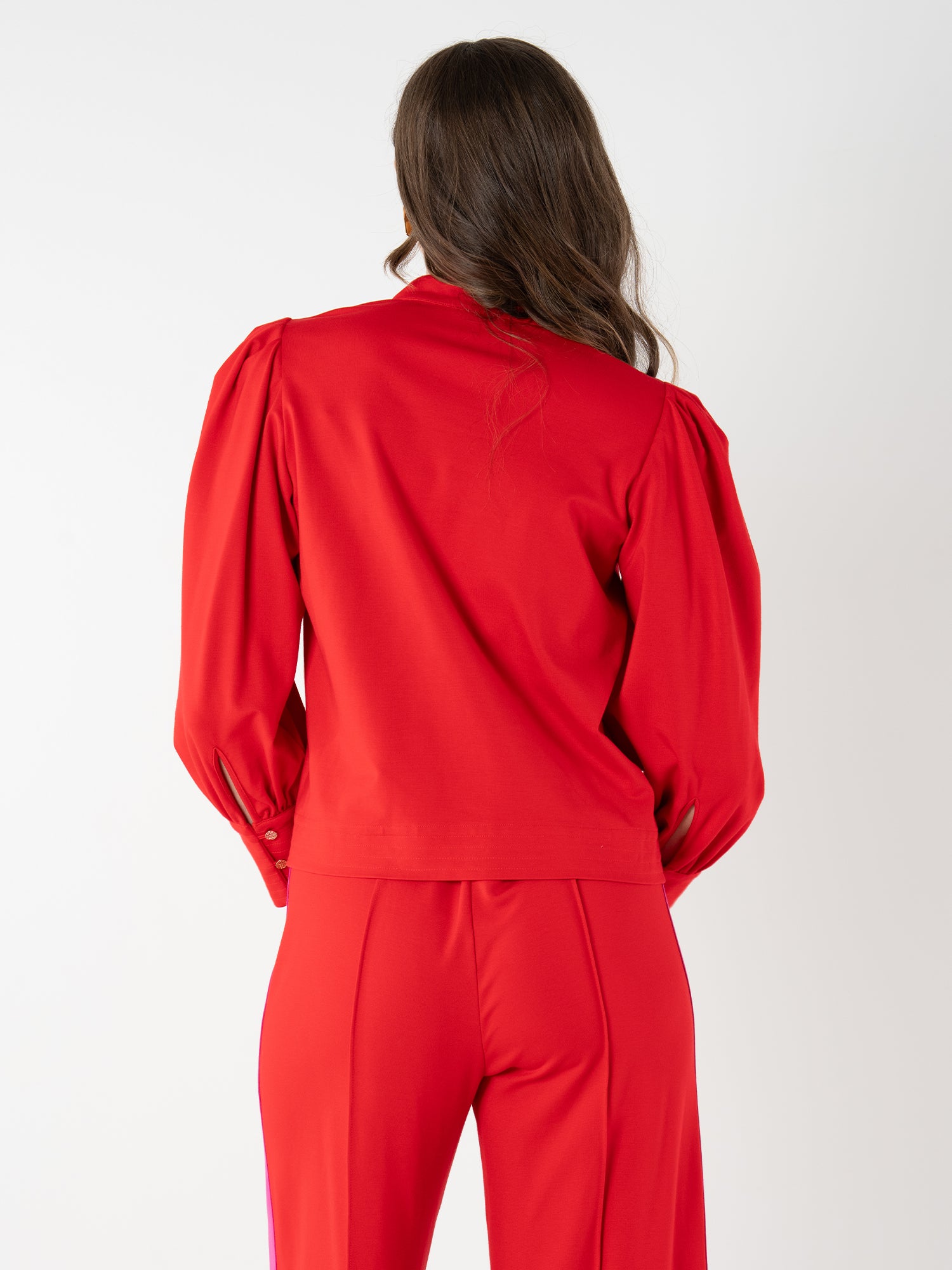A woman with long brown hair, seen from behind, wears a bright red Hampton Top with a mandarin collar and puffed shoulders, paired with matching high-waisted pants against a plain white background.