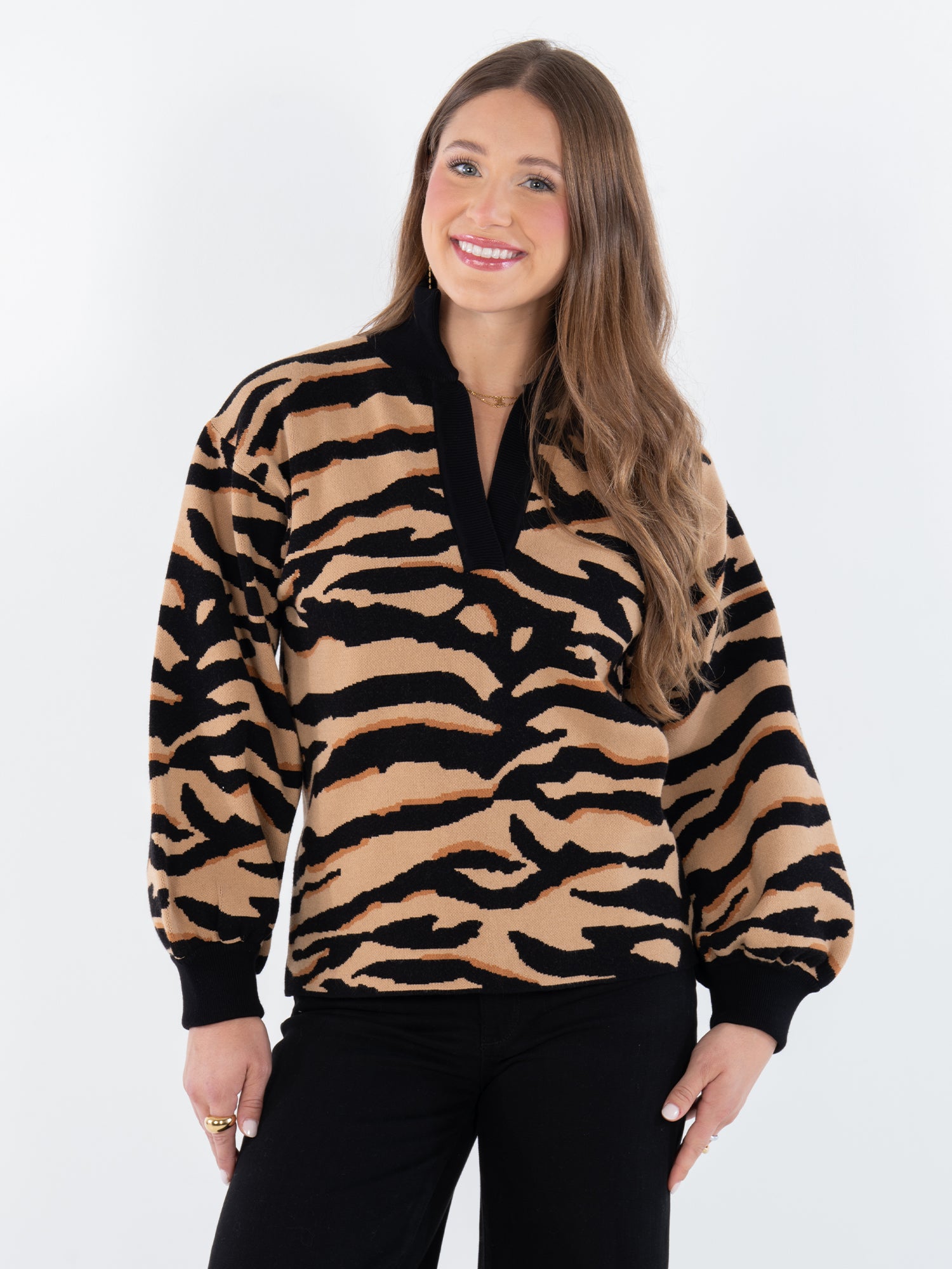 A woman with long brown hair wears the Lolli Sweater featuring a Lady Tiger print with black cuffs and collar, paired with black pants. She smiles against a white background, showcasing the vintage charm of the Lolli Sweater.