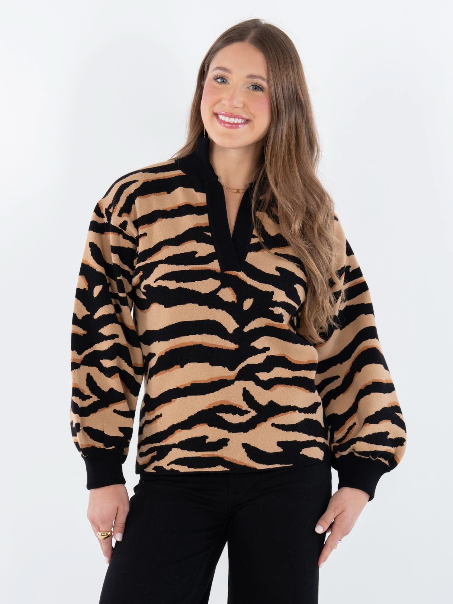 A woman with long brown hair wears the Lolli Sweater featuring a Lady Tiger print with black cuffs and collar, paired with black pants. She smiles against a white background, showcasing the vintage charm of the Lolli Sweater.