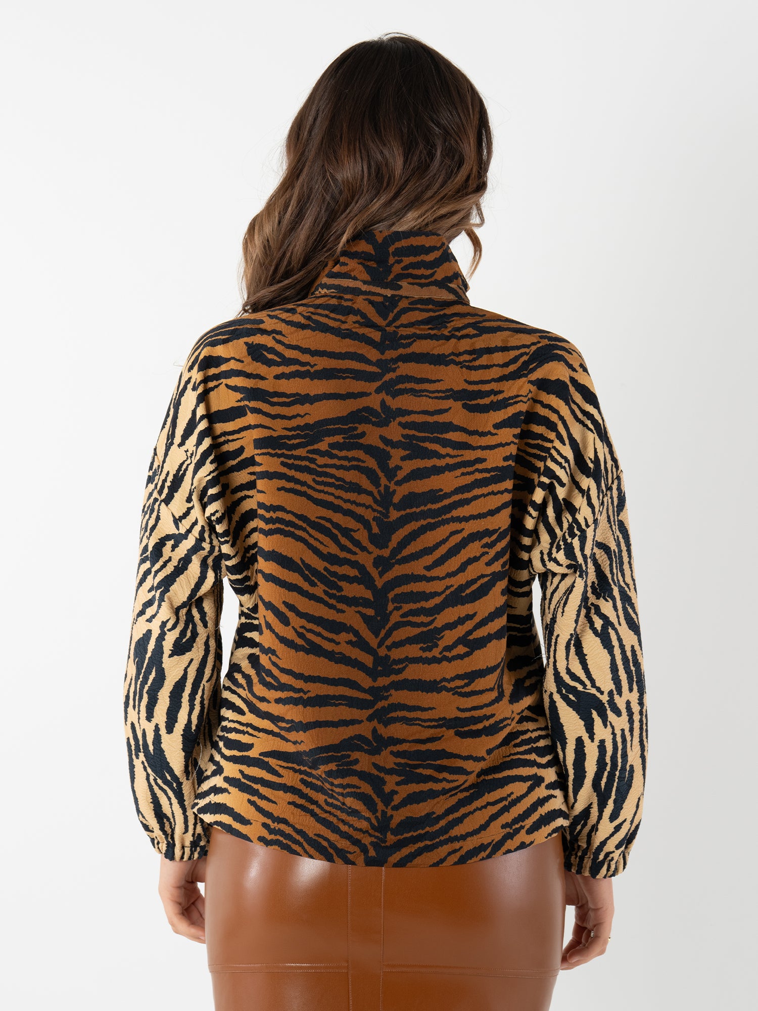 A woman with long brown hair, seen from behind, wears the Long-sleeve Poppy and a brown leather skirt inspired by vintage Italian interiors, set against a plain white background.