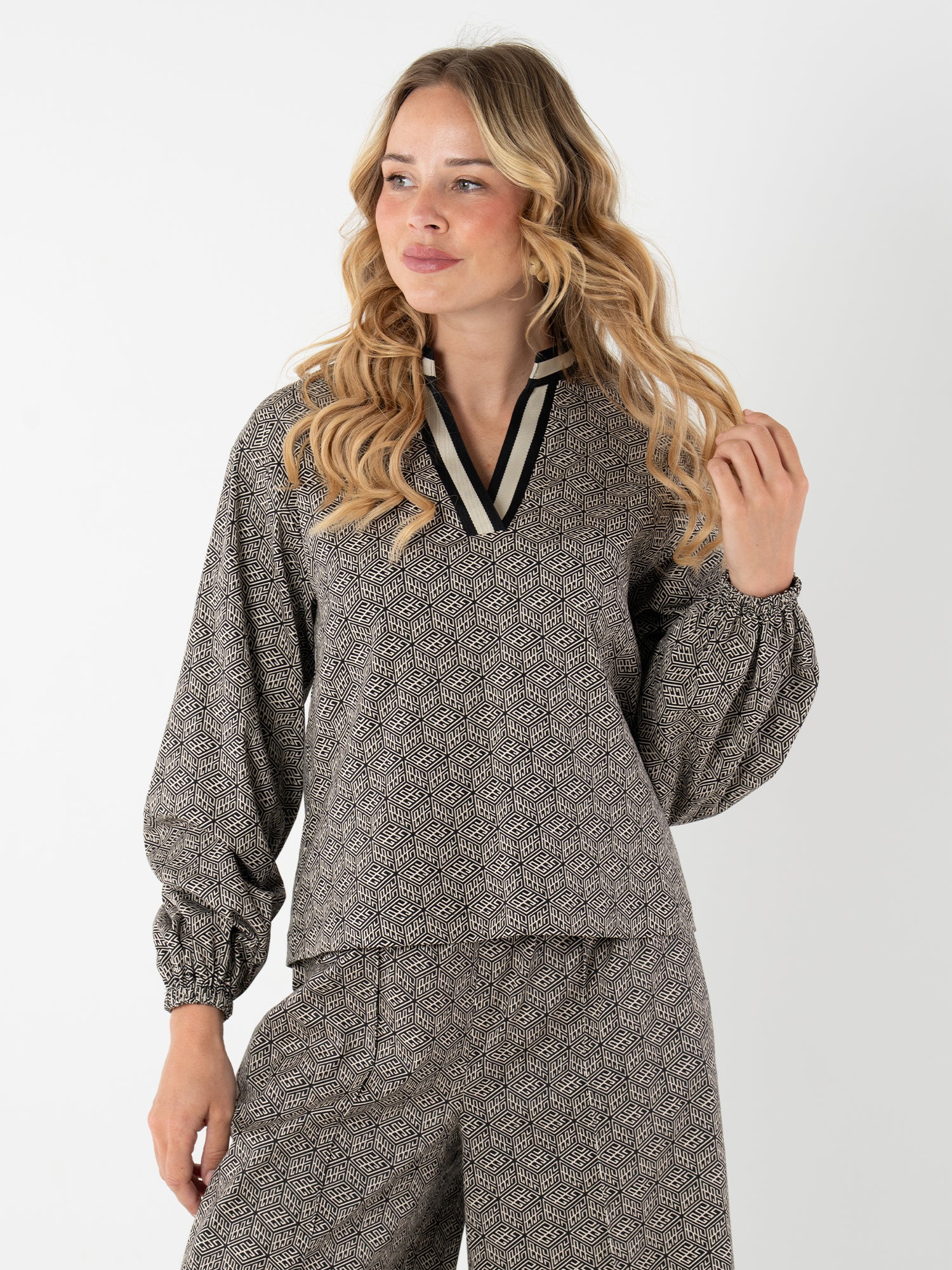 A woman with long blonde hair wears the Lolli Top, a grey patterned blouse with black monogram and relaxed dolman sleeves, paired with matching wide-leg pants against a plain white background.