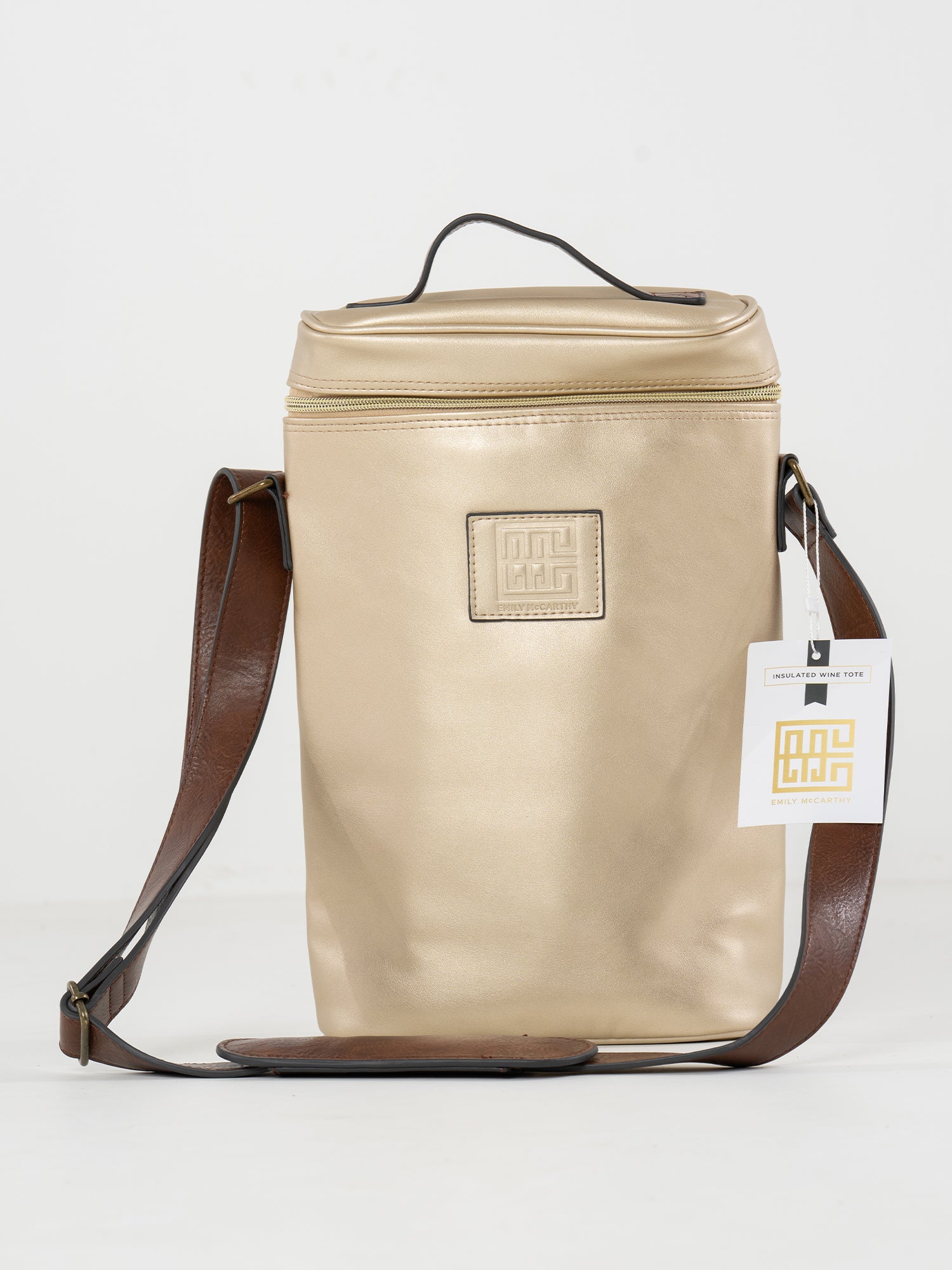 The Insulated 2-Bottle Wine Bag is a gold rectangular leather tote with a top handle, brown adjustable shoulder strap, front logo patch, and branded tag on the strap, displayed against a plain white background.