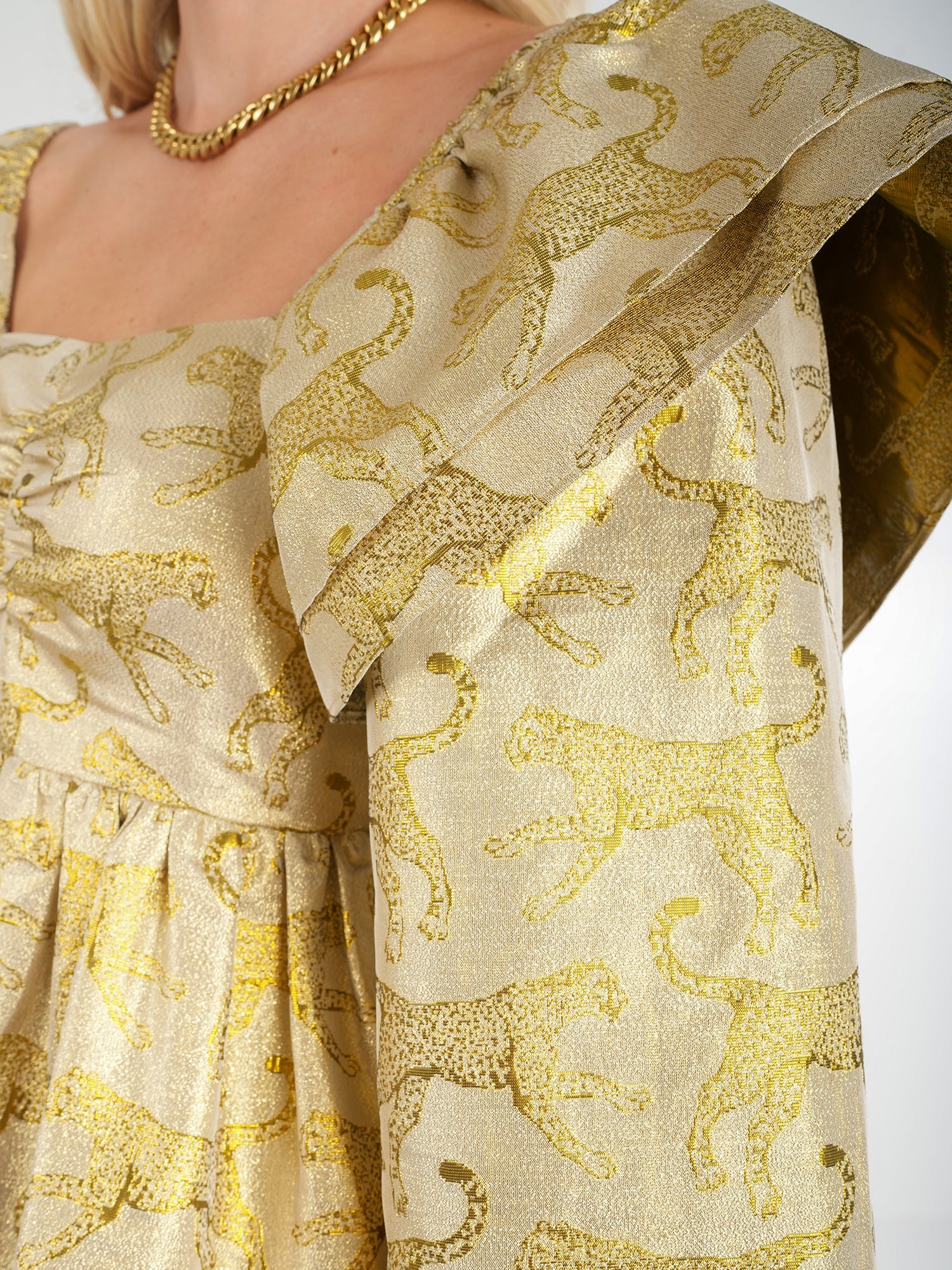 Close-up of an individual styled in the eye-catching Gigi Dress - Jaguar Jacquard, showcasing its distinctive large, ruffled shoulder design and complemented by a chunky gold necklace.