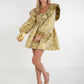 A woman in a Gigi Dress - Jaguar Jacquard, characterized by voluminous sleeves, poses against a white background with a matching clutch. She completes her look with nude heels and a gold necklace, while her long hair cascades in waves.