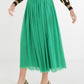 A person is wearing the Misty Maxi - Jolly Green skirt paired with a leopard print sweater and a velvet waistband. The skirt flows gracefully, and they have completed the outfit with metallic-finished pointed heels for an elegant touch. The background features a plain white wall.