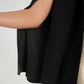 Close-up of a person wearing the Overlay Cape - Silent Night, a sleeveless black top with a flowing cape design at the shoulder, paired with metallic gold pants. The image focuses on the side view of the garment and the model's arm against a neutral background.