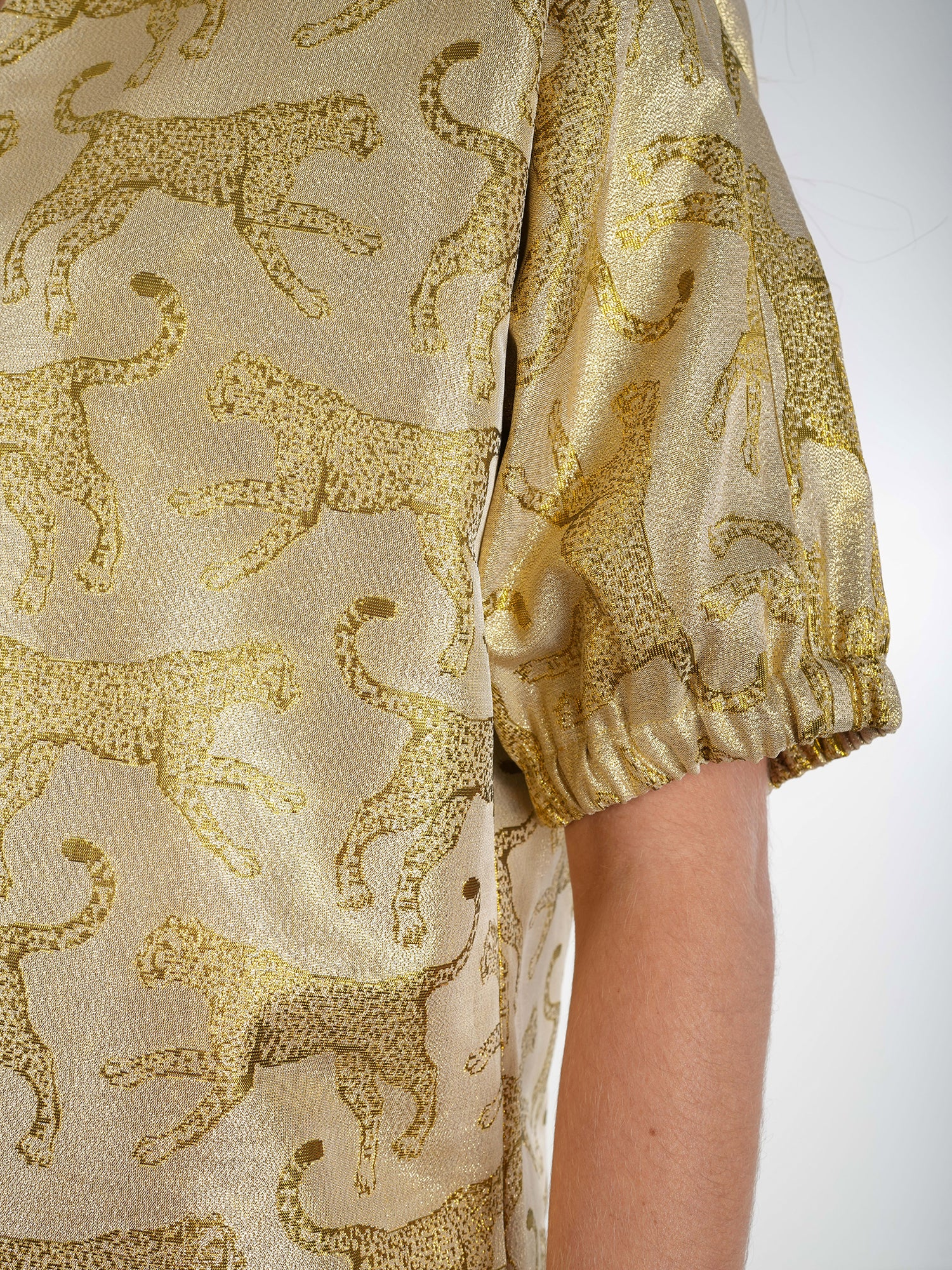 Close-up of a person wearing the Poppy Dress in light golden-brown with a jaguar jacquard pattern, highlighted by short, puffed sleeves that evoke the elegance of wild felines.