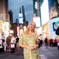 A woman in a stunning Poppy Dress - Jaguar Jacquard poses confidently in a bustling Times Square at dusk, surrounded by bright billboard lights and people.