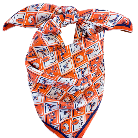 The Gameday Scarf - Orange & Navy Checkerboard showcases a white and blue geometric pattern, complete with horses, football helmets, and Broncos text. Ideal as a scarf or trendy hair accessory, it is neatly folded and tied at the top.