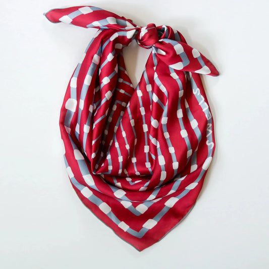 The Gameday Scarf - Crimson & Grey is elegantly tied in a knot at the top, beautifully showcased against a plain white background. It features hand-sewn craftsmanship with red silk and white and gray geometric patterns, crafted with care in Montreal, Canada.