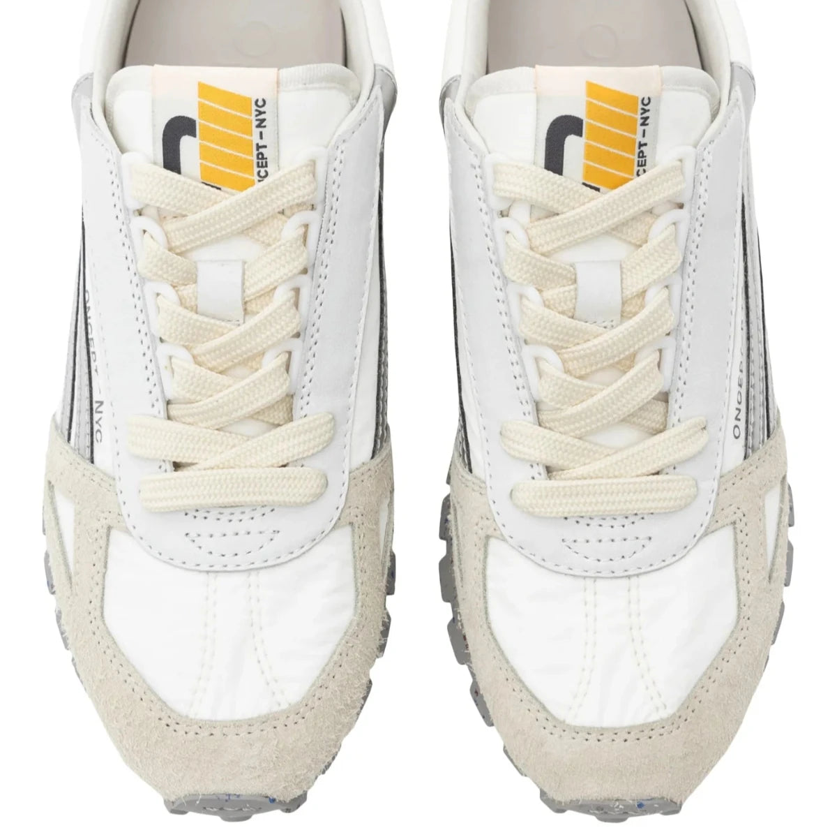 A top-down look at the Toronto Silver Splash Sneakers reveals their white and beige design, accented by black stripes. The tongue features distinctive yellow and gray tags with the text "CONCEPT NYC." These hybrid sneakers are designed for lightweight comfort and support, complete with textured soles and white laces.