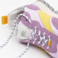 Close-up of the Osaka Lilac Haze Re-Nylon shoe highlighting its purple suede, yellow accents, and white mesh. This Osaka-inspired sneaker features black-and-white speckled laces, a rugged gray sole with a platform midsole, and orange fabric details. The tongue displays a visible white tag with text.