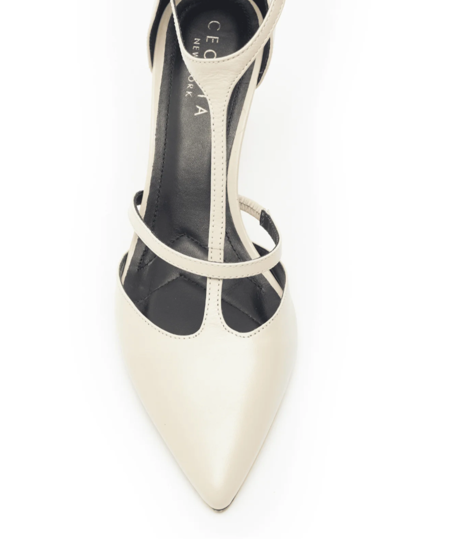 The Crawford Heel - Beige Lizzard is an elegant high-heeled shoe featuring a pointy toe in off-white leather with thin T-straps across the arch. The black insole displays white branding, and the stiletto heel is photographed from above on a white background.