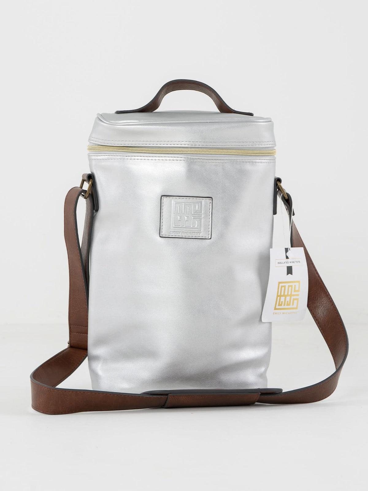The Insulated 2-Bottle Wine Bag is a sleek metallic silver shoulder bag with a brown strap, square embossed logo, top zipper, small handle, and a white tag on the strap. Shown on a plain white background.