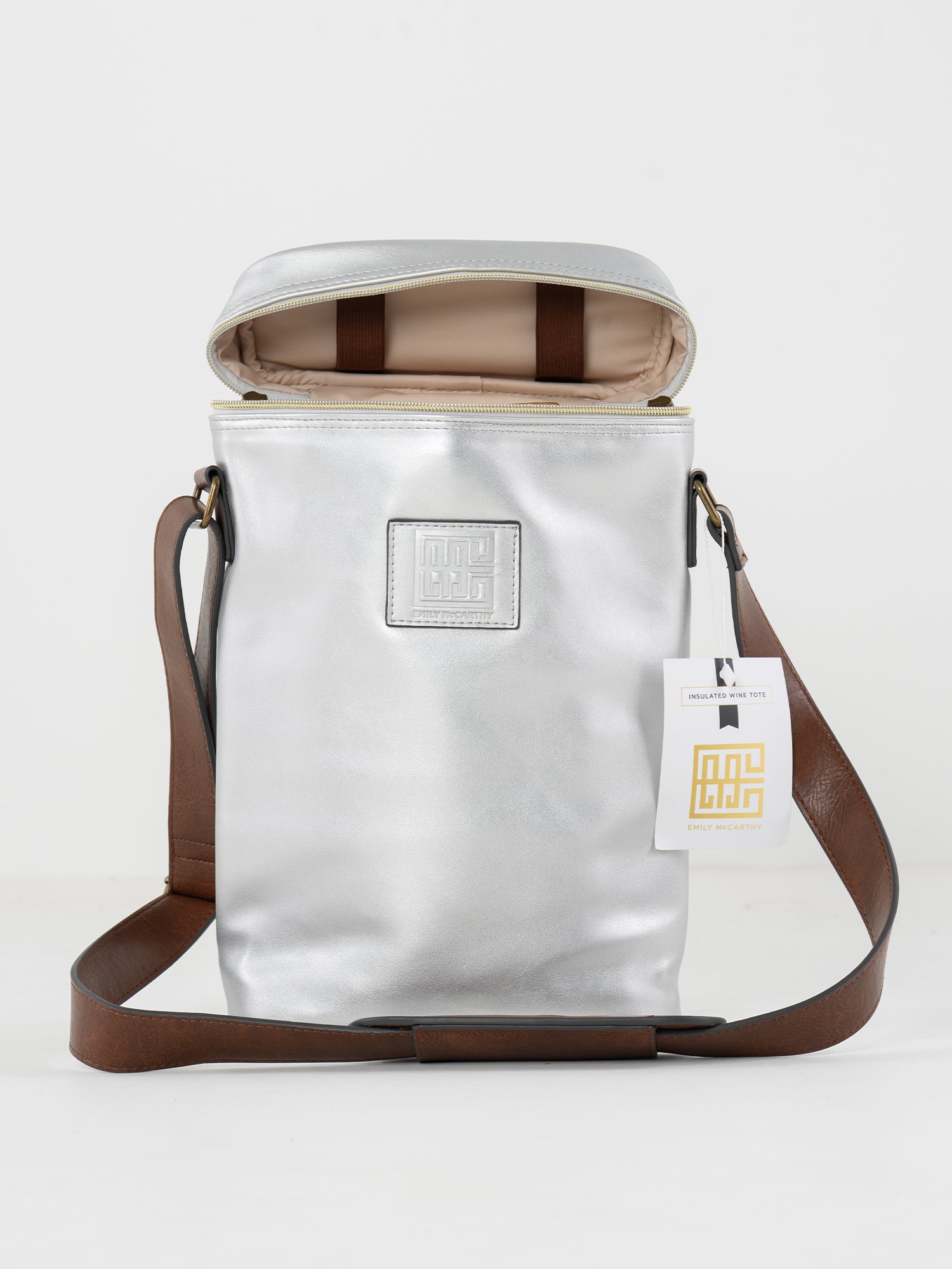 The Insulated 2-Bottle Wine Bag features metallic silver exterior, brown strap, partially unzipped to show beige interior, a square logo patch on the front, and a white tag with gold and black details—stylish and functional.