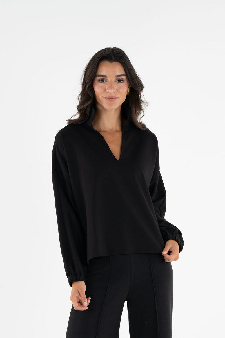 A woman modeling a black long-sleeve V-neck top and matching black wide-leg trousers against a plain white studio background.