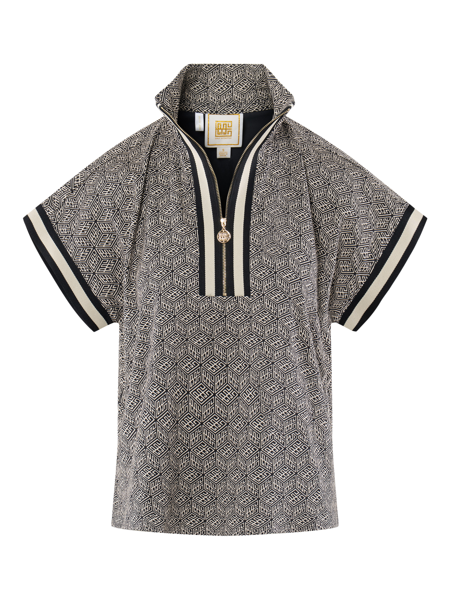 The Poppy Pullover is a chic short-sleeve women’s top featuring a black and white geometric pattern, partial front zipper with round gold pull, and beige and black trim on the sleeves and collar.