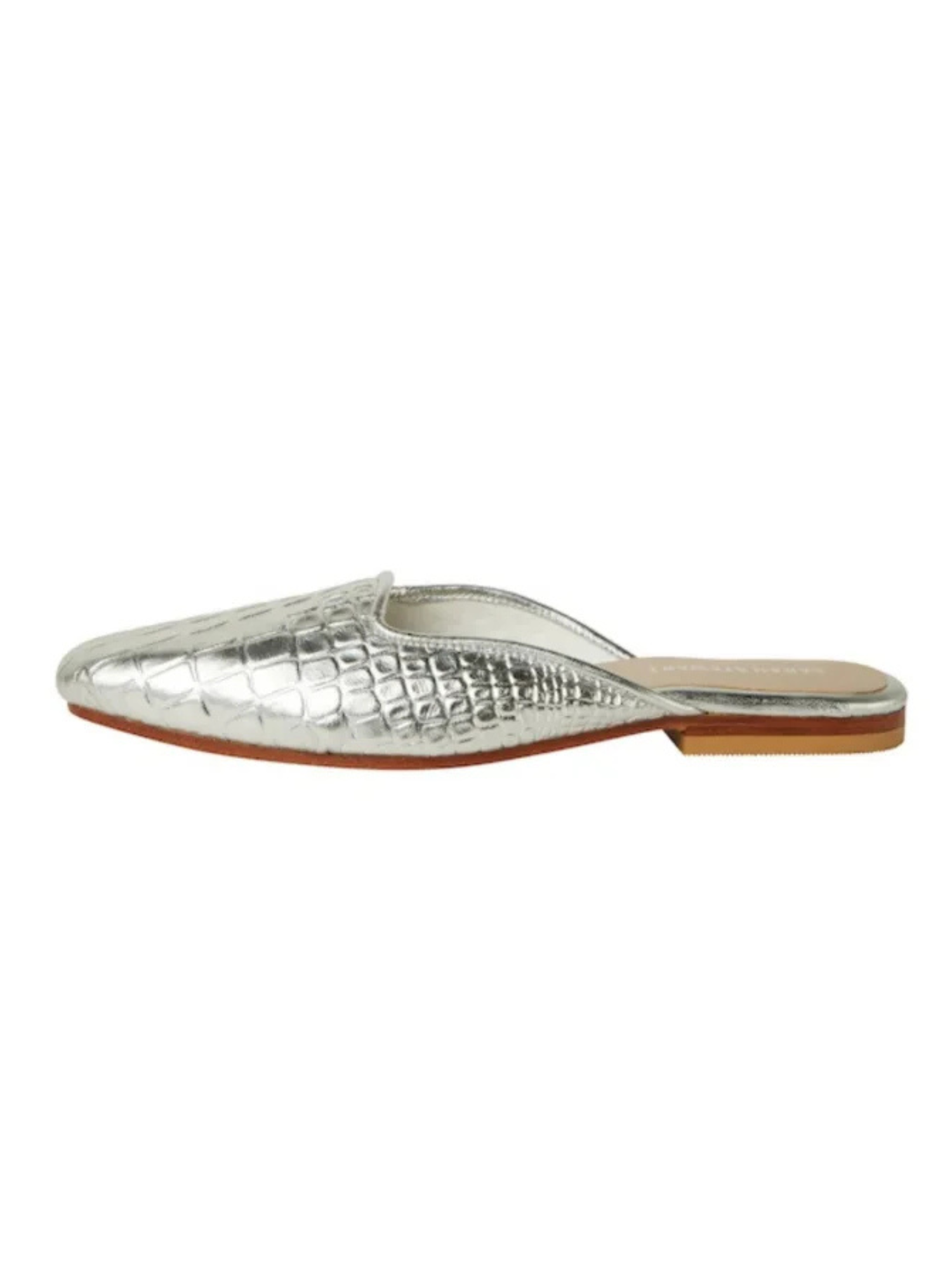 The Clara Mule - Silver showcases a crocodile pattern and hand-printed leather, with a flat brown sole. This slip-on shoe is elegantly displayed from the side against a white background.