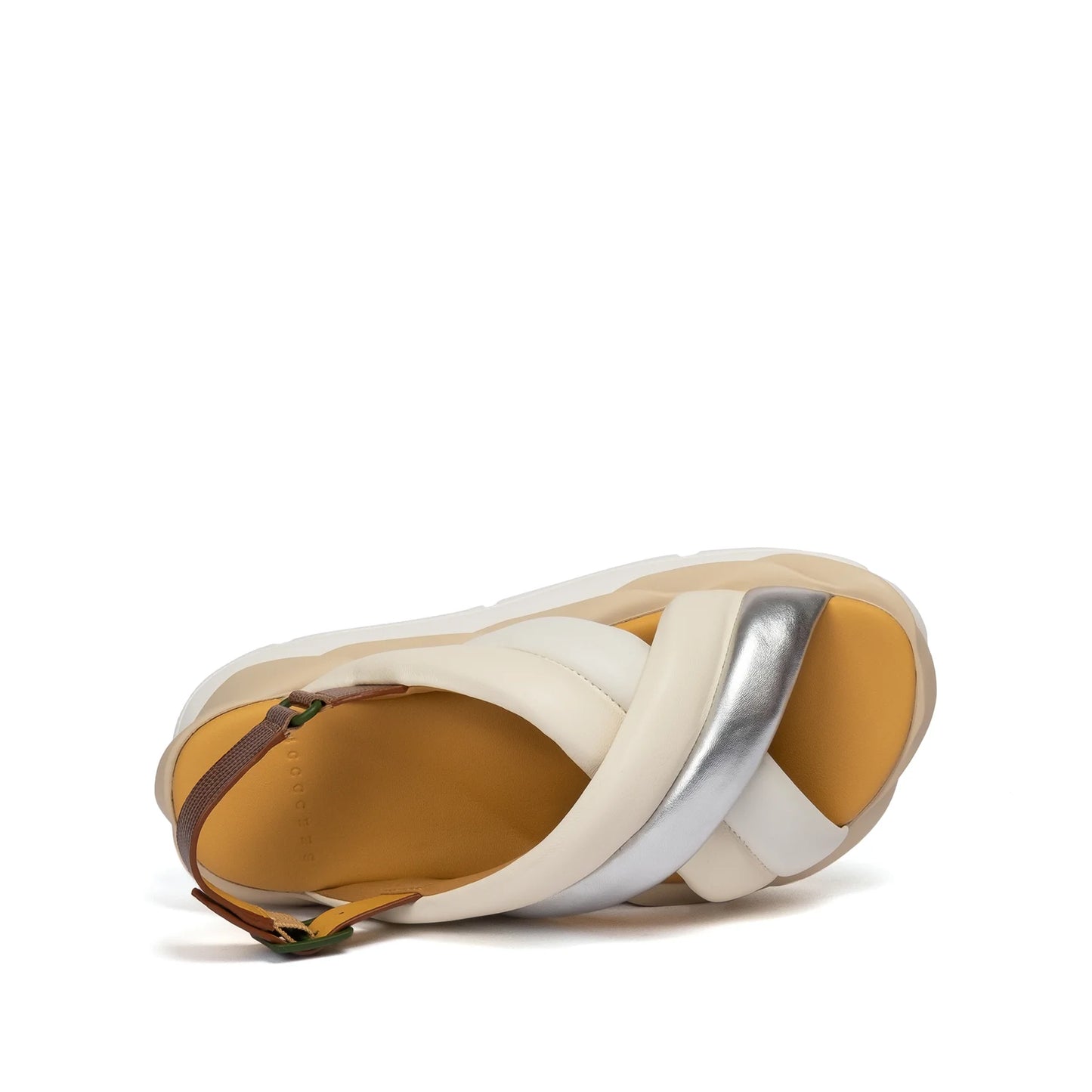 Introducing the Mellow Mela in Cream: a chic sandal showcasing crisscrossed straps in a blend of white and metallic silver, complemented by a tan padded footbed. It also features an adjustable slingback ankle strap with a brown buckle, all displayed against a simple white background.