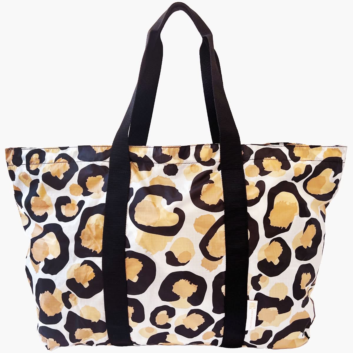 The Travel Tote - Classic Spot Cheetah boasts a striking leopard print design in shades of black, brown, and tan. It features durable black handles and a roomy interior, making this chic tote ideal for carrying your daily essentials.