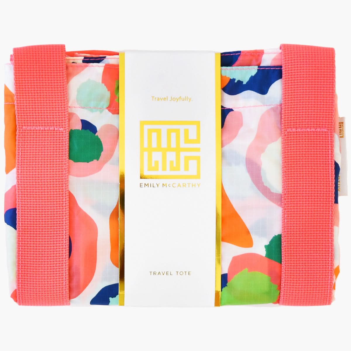 Introducing the Travel Tote - Multi Spot Cheetah from the Emily McCarthy Collection, this vibrant and durable accessory showcases abstract patterns in pink, orange, green, and blue. It features two wide pink handles running vertically. The central label proudly displays "Travel Joyfully" and "Emily McCarthy" in gold text, topped with a geometric logo.