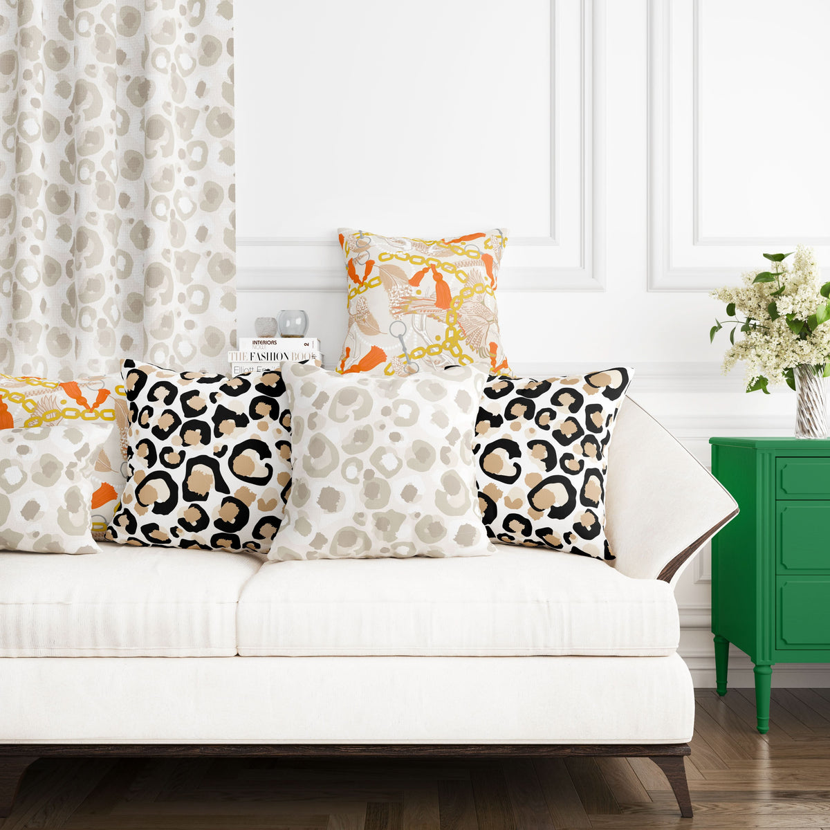 A white sofa upholstered in a cotton and linen blend is adorned with four patterned pillows, including designs using fabric named Classic Cheetah. In the background, a matching curtain complements the decor, while a green cabinet stands nearby, showcasing white flowers in a vase. The room is elegantly set off by classic white walls featuring molding details.