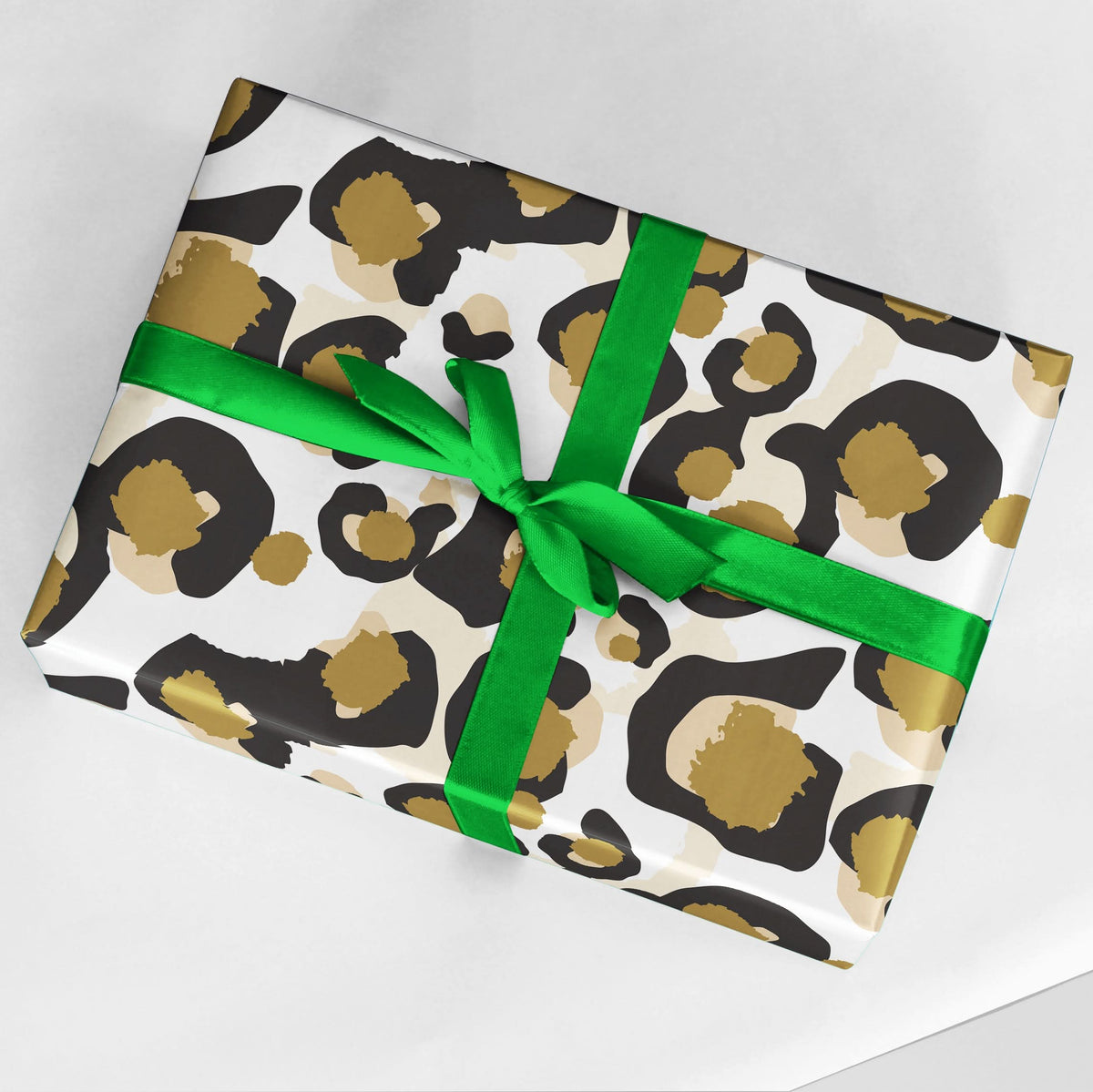 A gift box adorned in Classic Cheetah white paper, featuring a striking brown and black abstract pattern, is elegantly tied with a vibrant green ribbon in a bow and set against a white background.