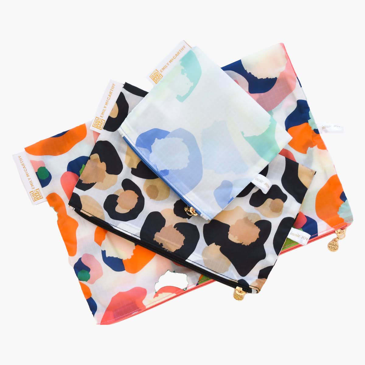 Three zipper pouches from the Cosmetic Carryall Set - Cheetah Mix, featuring vibrant abstract patterns akin to Emily McCarthy's style, are stacked gracefully. Each pouch showcases a distinct design incorporating shades of orange, blue, green, and black, complemented by gold zipper pulls and branded tags.