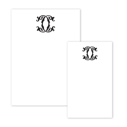 The Gift Bar Notepad Set includes two pieces of white stationery adorned with decorative black ornate designs at the top, reminiscent of elegant notepads. The intricate swirls and symmetrical patterns lend a touch of sophistication, with the sheets differing in size and the larger one gracefully positioned on the left.