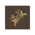 The Sporting Luxe Cocktail Napkins showcase two pheasants on crossed branches with antlers and a shotgun shell in gold foil, forming a striking crest on a textured dark brown background.