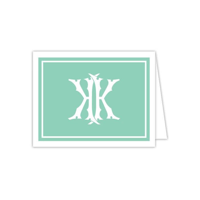 The Gift Bar - Folded Note set includes 10 notecards with a teal background, highlighted by an ornate white monogram design at the center with intricate shapes and decorative elements. Each card is framed by a white border and comes with matching envelopes for a polished presentation.