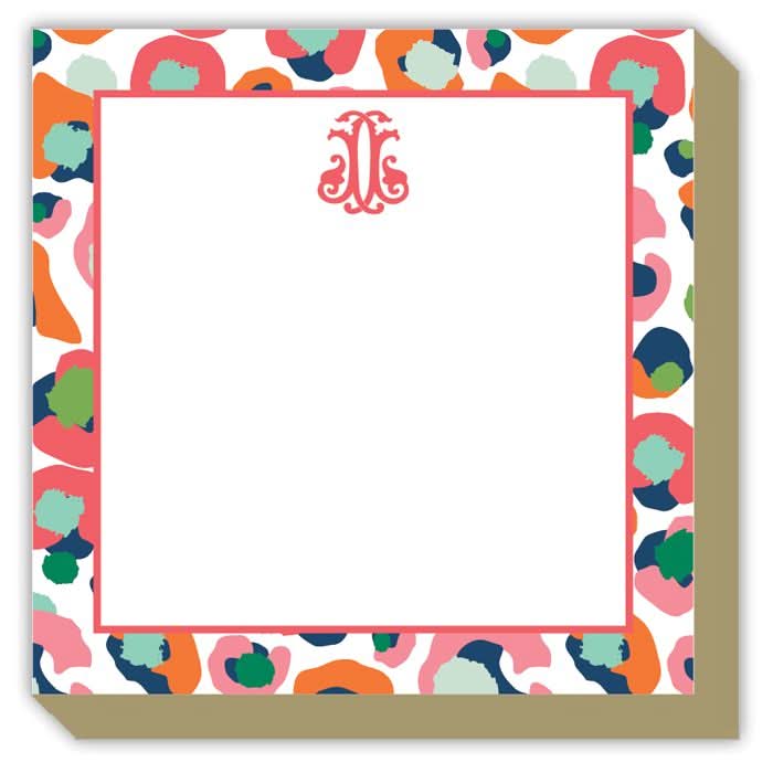 The Gift Bar - Luxe Notepad is a square notepad measuring 5.5 x 5.5 inches, designed with a vibrant abstract border featuring shades of pink, green, blue, and orange. The center is white and includes a decorative pink monogram at the top. It contains 65 sheets of premium paper perfect for all your notes and doodles.